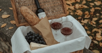 Picknickkorb mit Rotwein, Baguette, Trauben und Käse im Herbstlaub